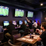 56WIN players cheering during a live sports betting event, surrounded by screens and betting slips
